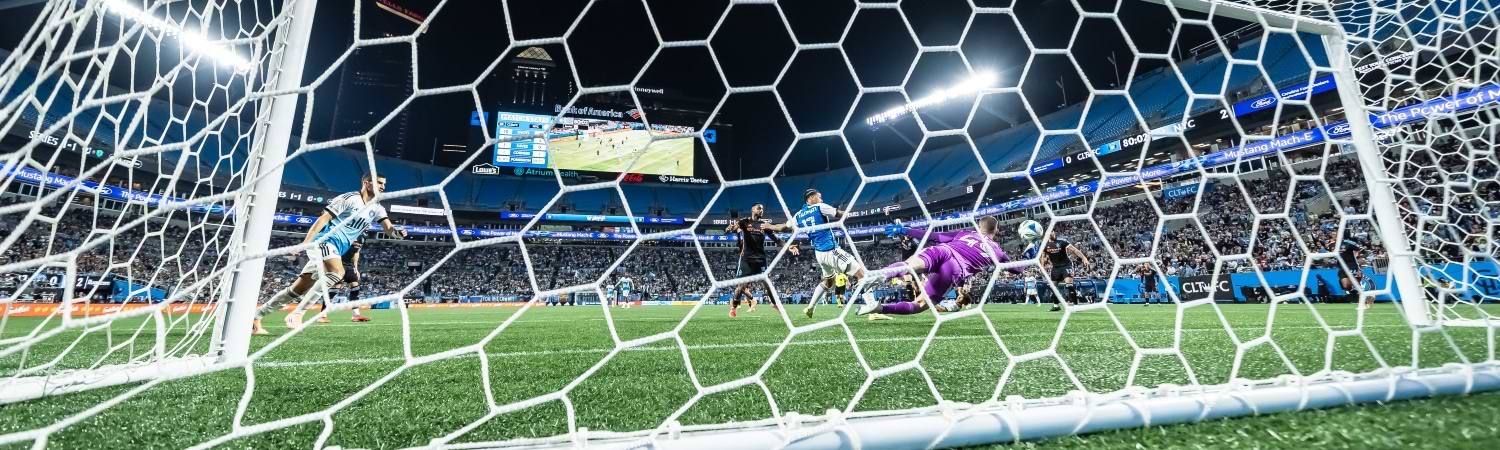 Porteria, en el fondo jugadores , tiro a portería y el portero se lanza al balón