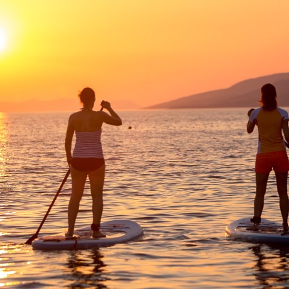 People paddle boarding at sunset