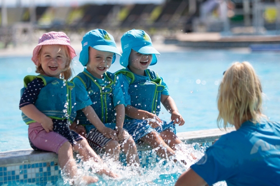 Three young children splashing in pool with nanny