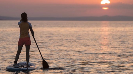 2 people stand up paddle boarding at sunset