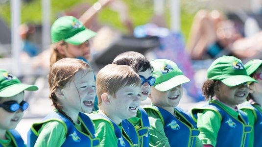 group of young children sitting along edge of swimming pool