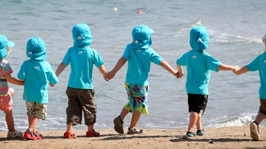 group of toddlers holdimg hands and walking along the beach