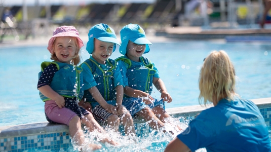 Three young children splashing in pool with nanny