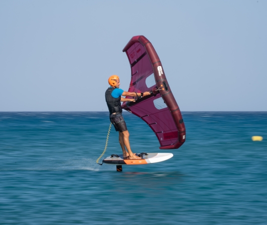 A man wingfoils with a helmet on a calm sea