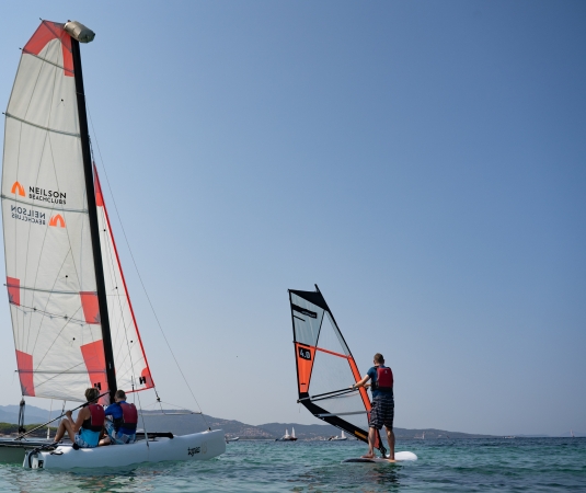 shows a calm sea scene with a catermaran and a windsurfer
