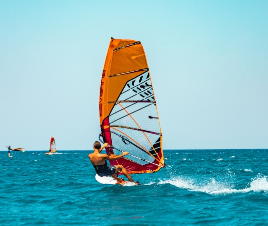 a person windsurfing on a clear, blue sea under a bright sky.
