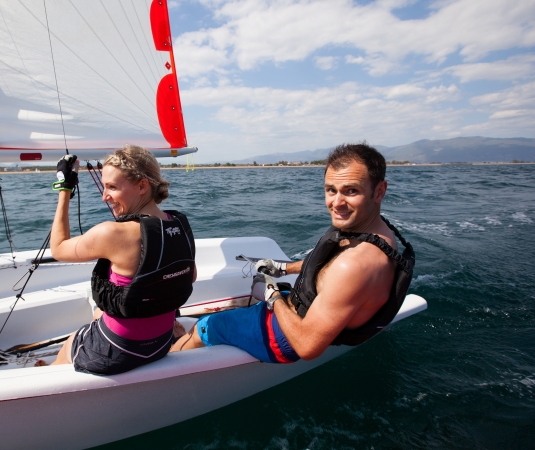  A man and a woman enjoying a sailboat ride on a partly cloudy day.