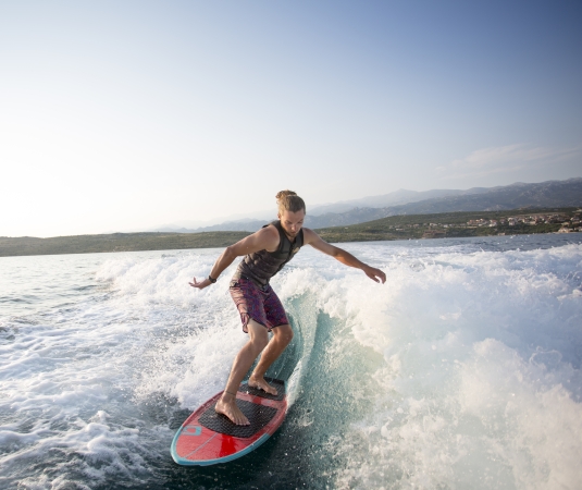 A man wakesurfing a large wave on a bright sunny day
