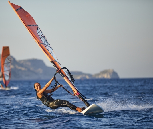 A woman windsurfing in a harness, with another windsurfer in the background