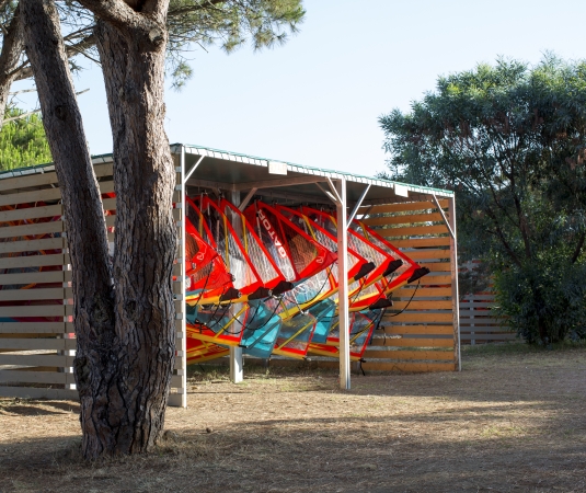 a neatly organized storage shed holding multiple windsurfing boards with colorful sails. 