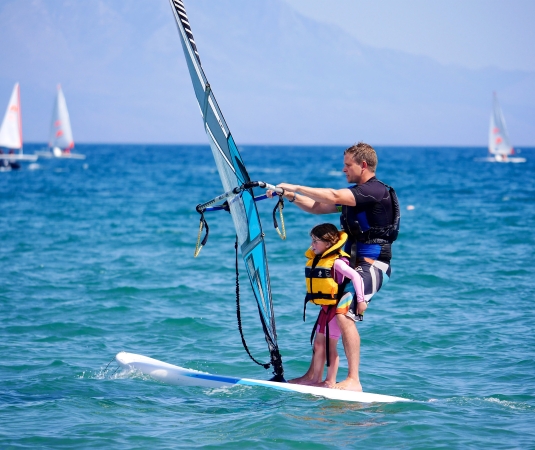 a man and a young child windsurfing together on calm blue waters.