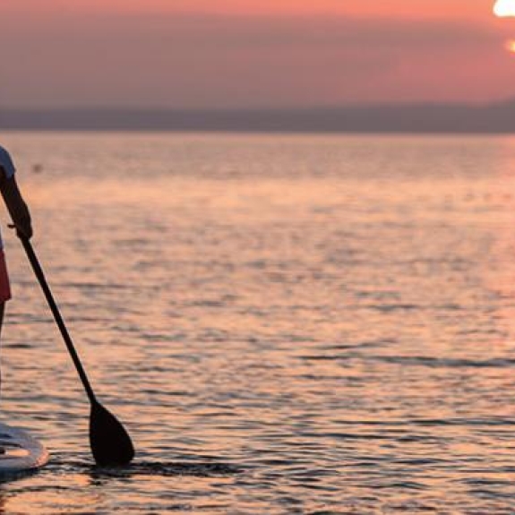 Two women stand up paddle boarding at sunset