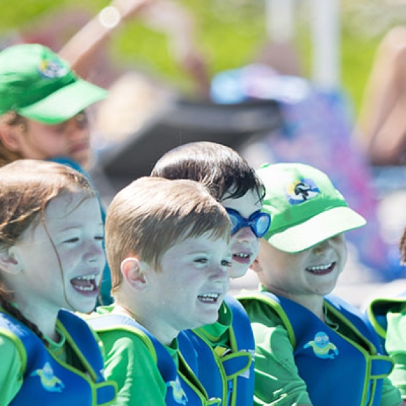 group of young children sitting along edge of swimming pool