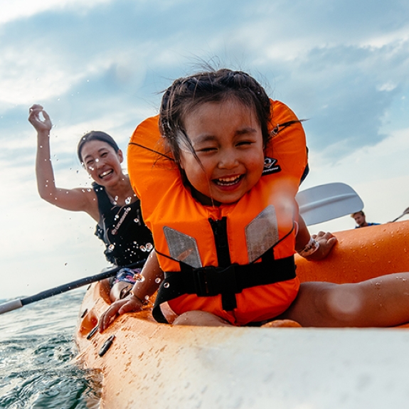 Young girl and woman splashing water and laughing in a canoe