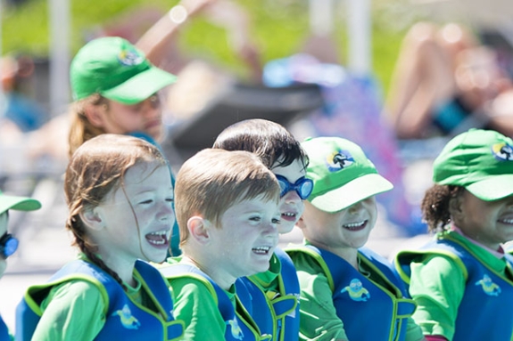 group of young children sitting along edge of swimming pool