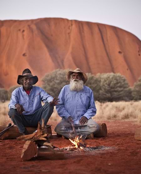To aboriginale mænd sidder ved et lille bål foran Uluru, Australien To aboriginale mænd sidder ved et lille bål foran Uluru, Australien