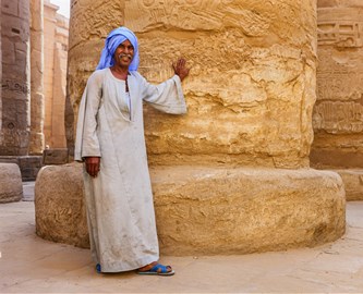 En mand i traditionel beklædning står ved foden af en søjle i Karnak-templet, Egypten