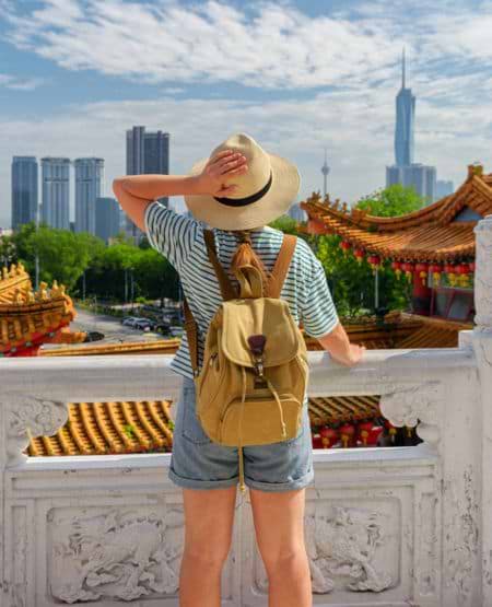 Kvindelig turist set bagfra kigger ud over temper og skyskrabere i Kuala Lumpur, Malaysia