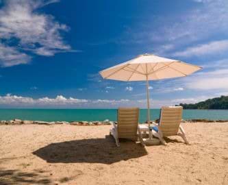To solsenge og en hvid parasol på sandstrand på Langkawi, Malaysia