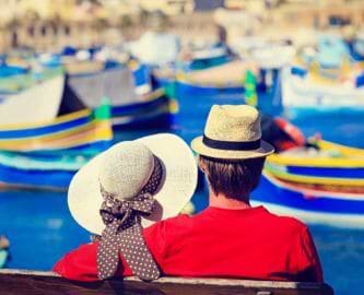 Par som sidder og kigger ud over havn med farverige både på Malta Par som sidder og kigger ud over havn med farverige både på Malta