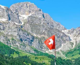 Schweizisk flag med sneklædte alpetinder i baggrunden, togrejse til Schweiz Schweizisk flag med sneklædte alpetinder i baggrunden, togrejse til Schweiz