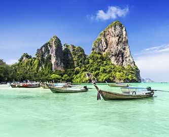 Traditionelle longtail-både i turkisblåt vand med dramatiske klipper i baggrunden, Thailand