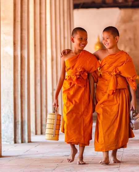 To unge buddhistiske munke, sandsynligvis novicer, klædt i traditionelle safranfarvede rober går i en søjlegang, Thailand