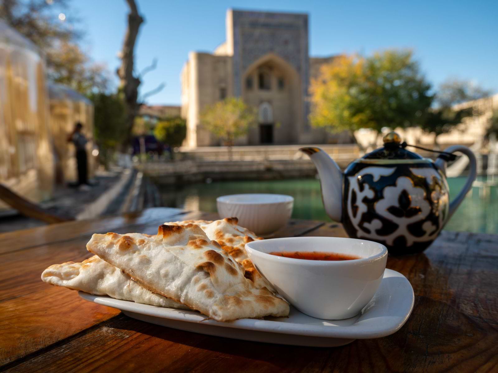 Te, samsa og tomat med Bolo Haouz-moskeen i Bukhara i baggrunden, Usbekistan