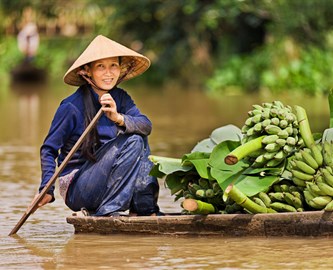 En kvinde med konisk hat sejler med bananer i Vietnam