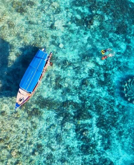 Badeferie på Bali: Lille båd i krystalklart vand set fra luften Badeferie på Bali: Lille båd i krystalklart vand set fra luften