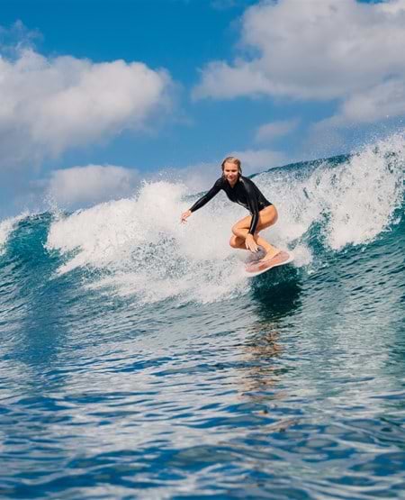 Kvinde som surfer i høje bølger på Bali Kvinde som surfer i høje bølger i Seminyak på Bali