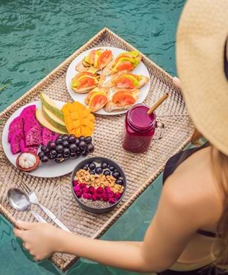 Kvinde med bakke med frugt og juice i pool på Bali
