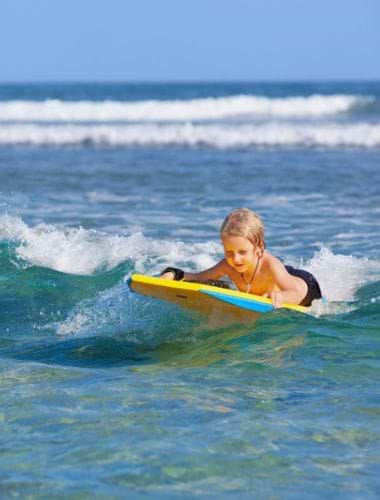 Mindre dreng surfer på bølgerne i havet ved Surfers Paradise, Australien