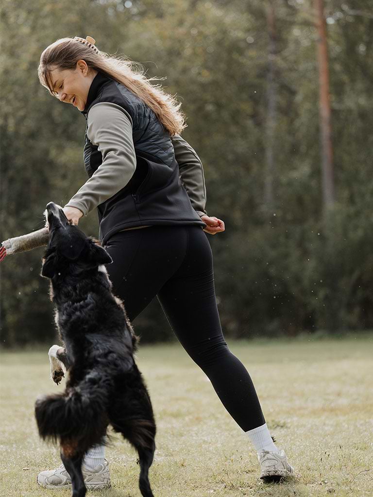 Woman playing with a dog in a black Misty Hybrid Vest.