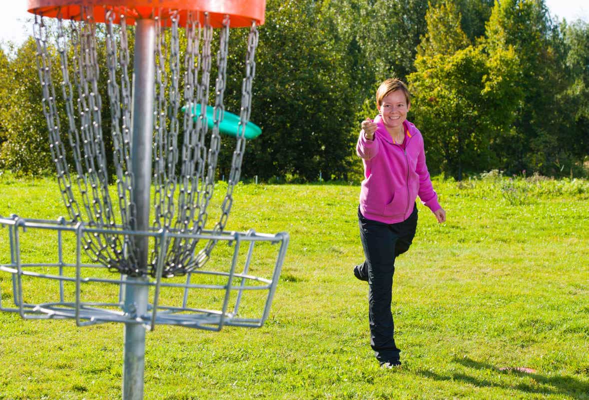 Female disc golfer putting into basket.