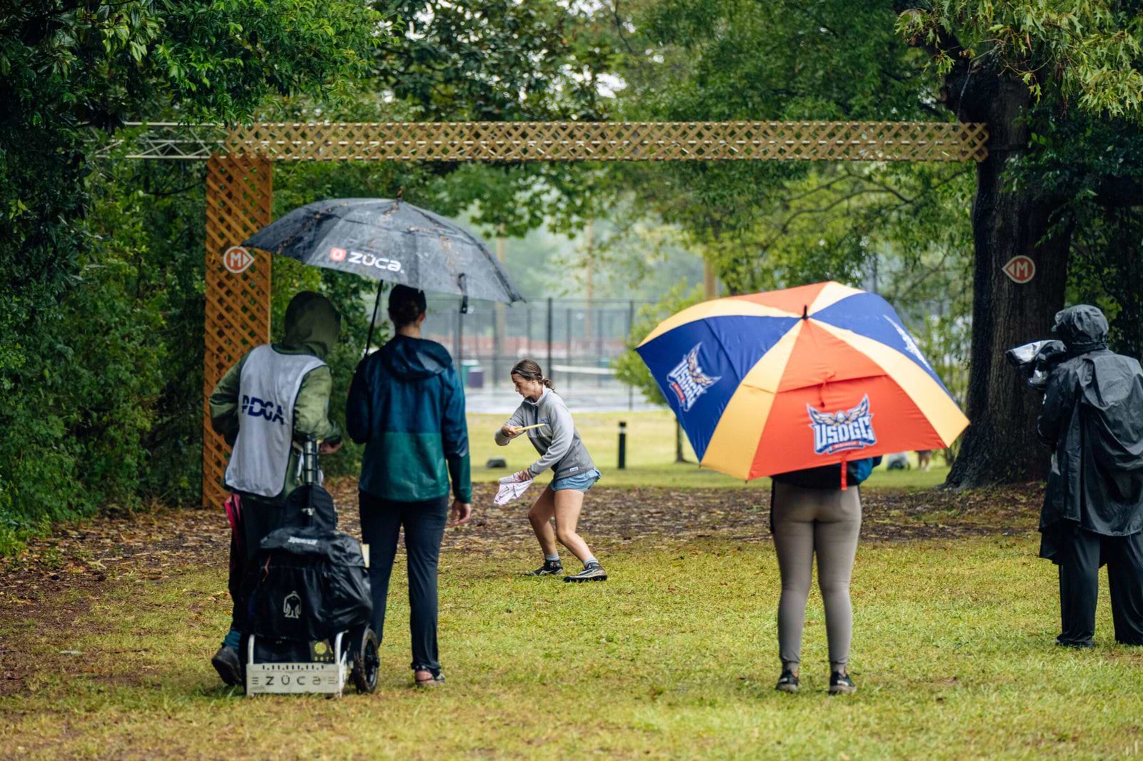 Throw Pink competitors and spectators gather under umbrellas beside a basket during Saturday’s third round.