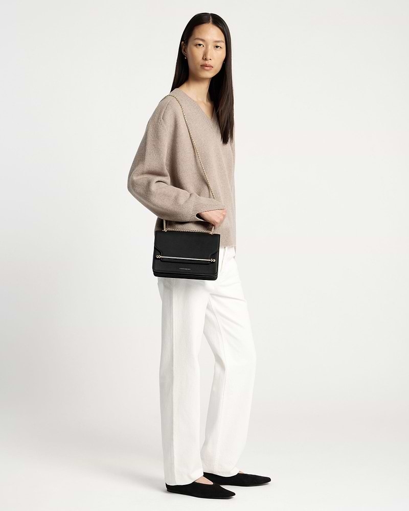 Model wearing black east-west shoulder bag with gold chain and boxy flap.