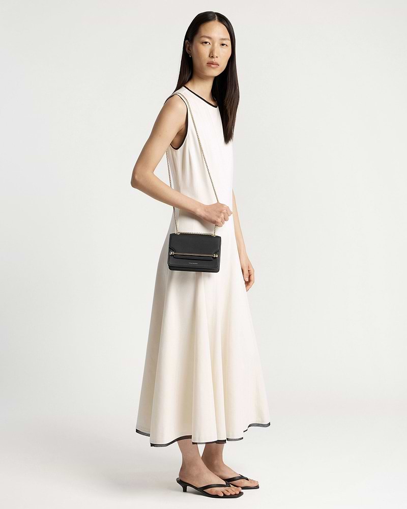 Model in a white sleeveless dress holding a small black crossbody bag with chain.