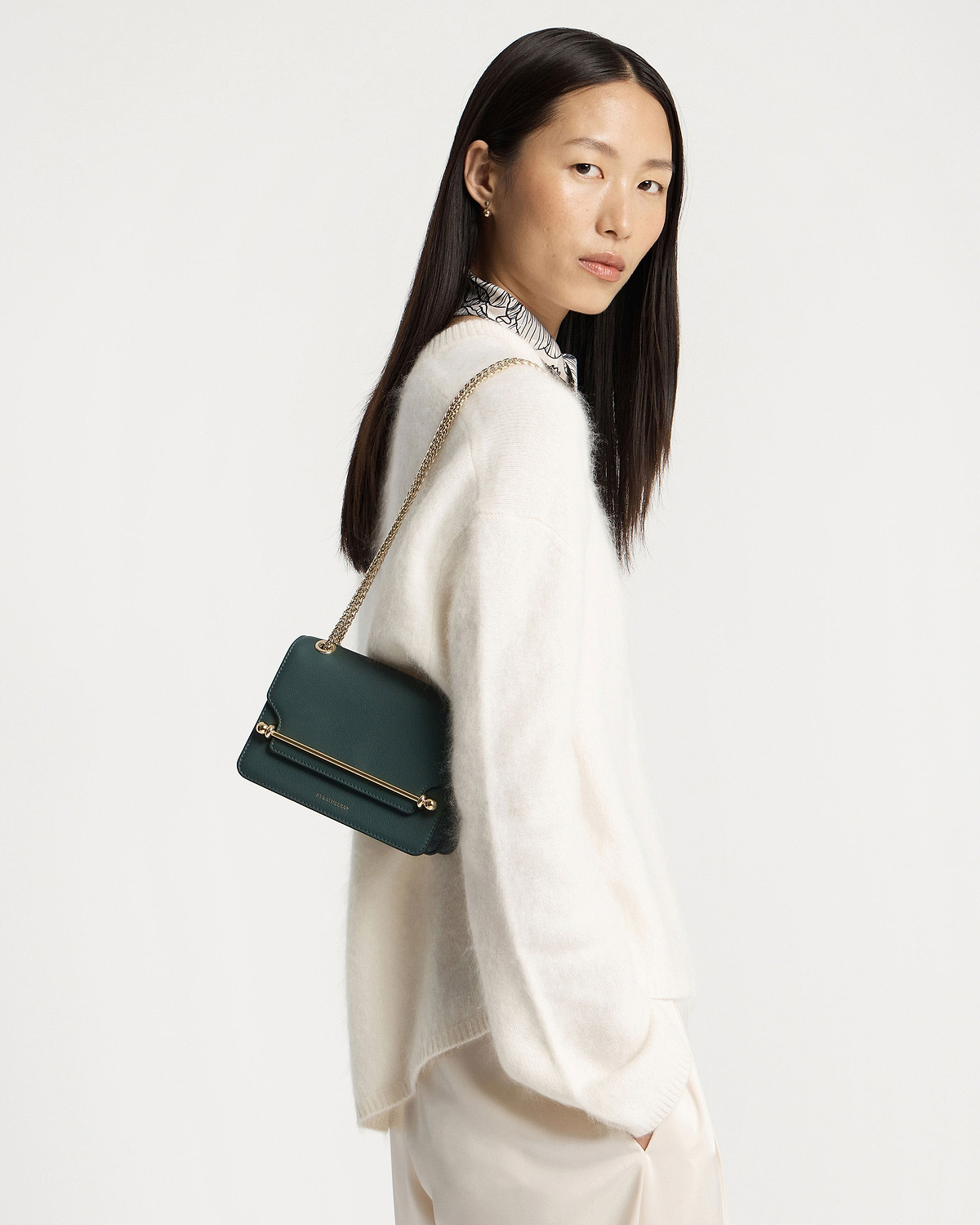 Woman wearing bottle green East/West Mini shoulder bag with gold bar detail.