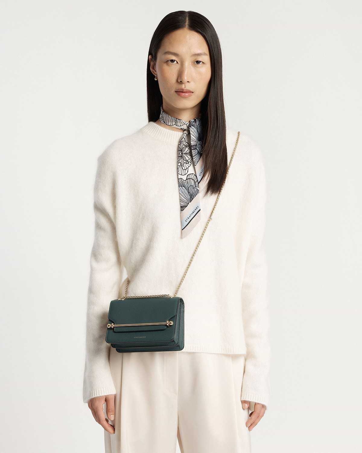 Model wearing cream jumper with bottle green East/West Mini bag and gold chain strap
