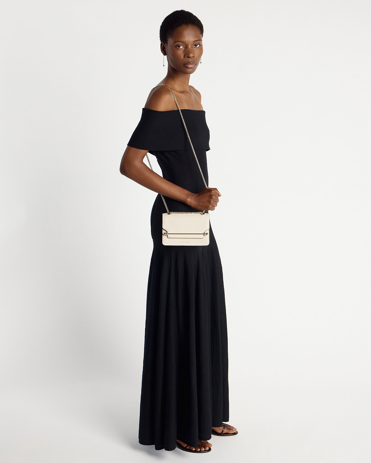 Model in black off-shoulder dress carrying a vanilla Strathberry East/West Mini bag.