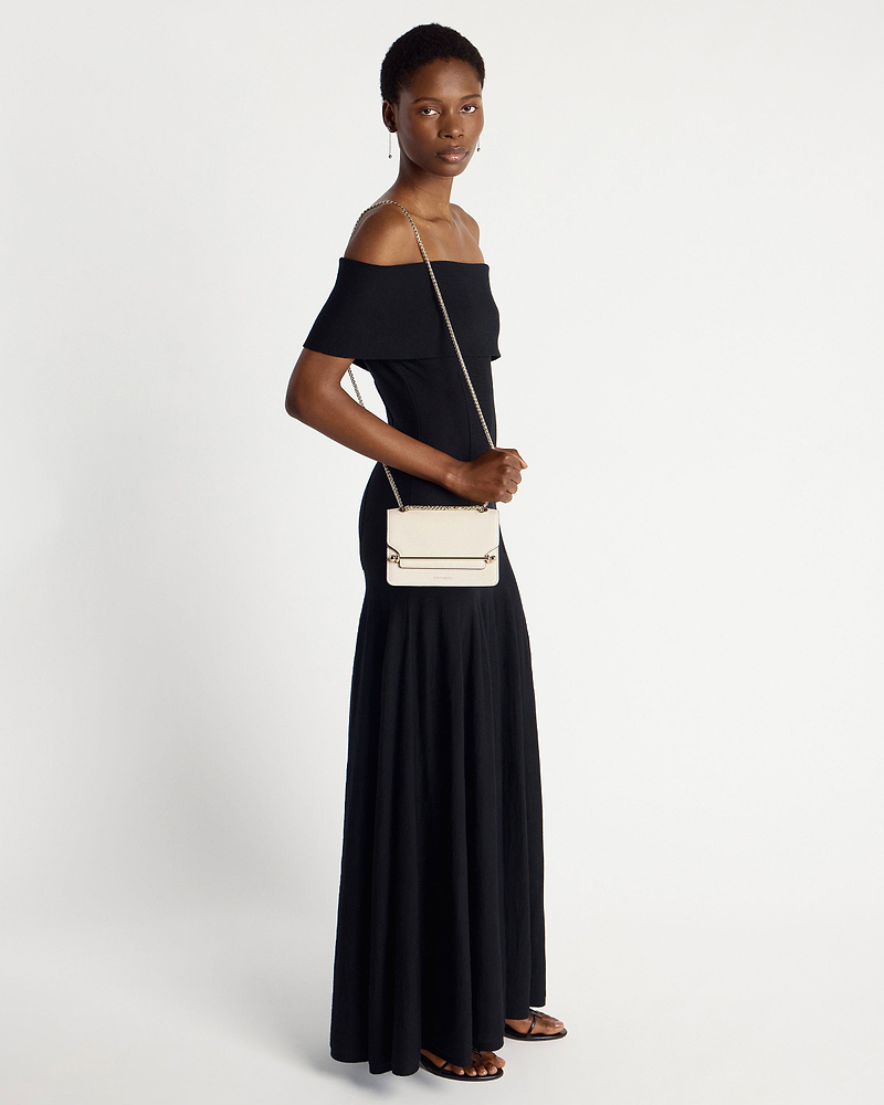 Model in black off-shoulder dress carrying a vanilla Strathberry East/West Mini bag.