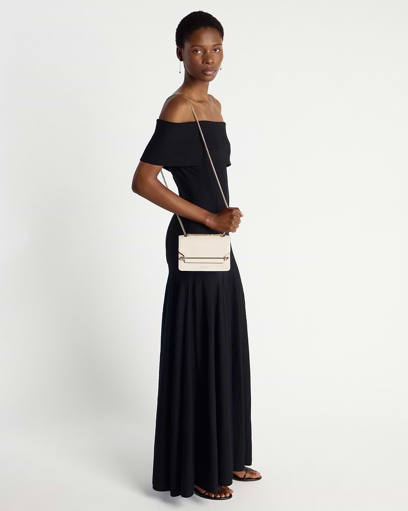 Model in black off-shoulder dress carrying a vanilla Strathberry East/West Mini bag.