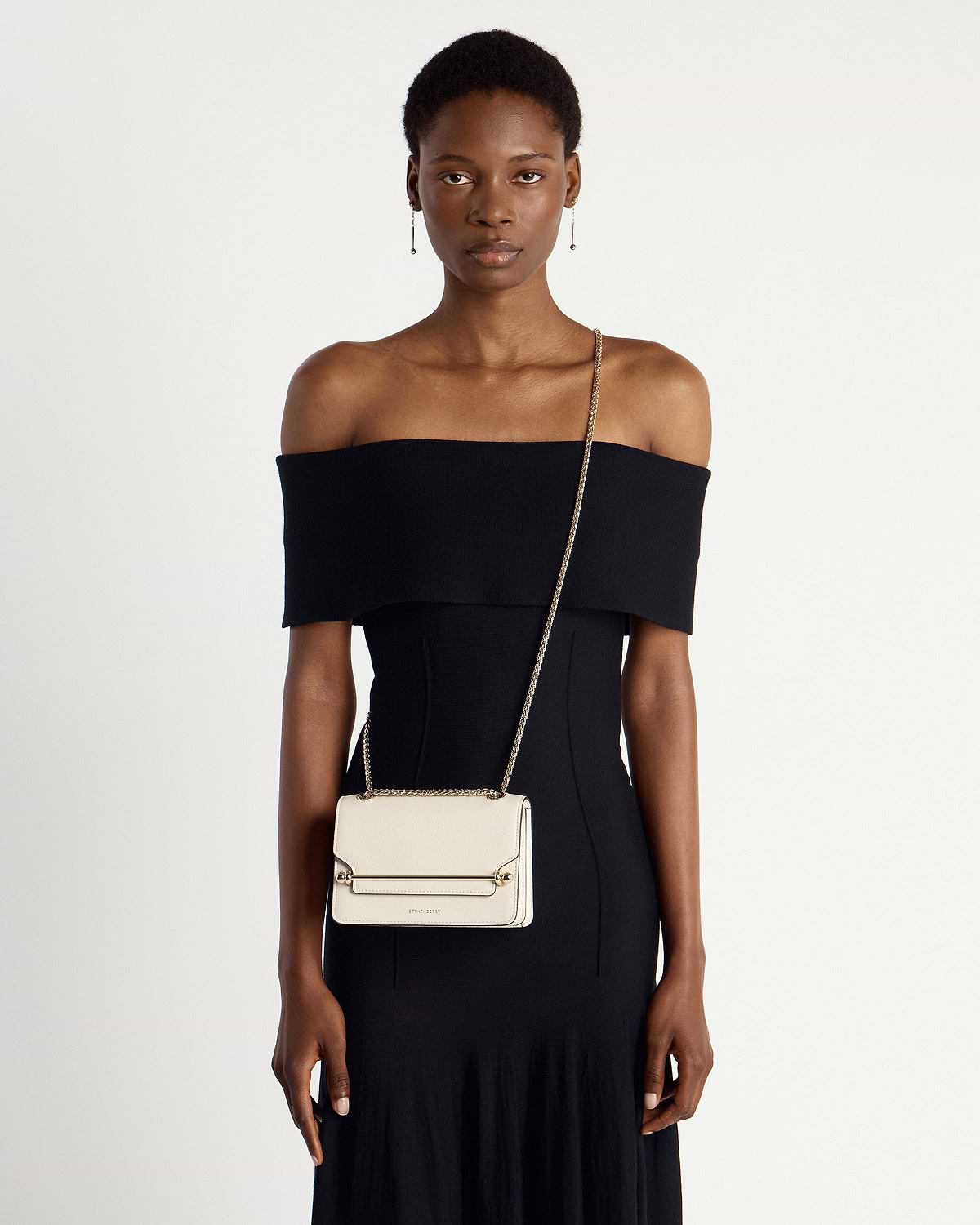 Model wearing a small vanilla crossbody bag with a gold chain strap.