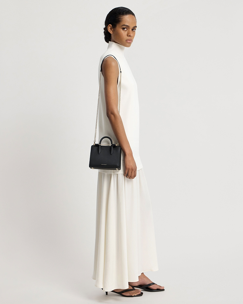 Model in a white sleeveless dress carrying a black nano tote with chain strap.