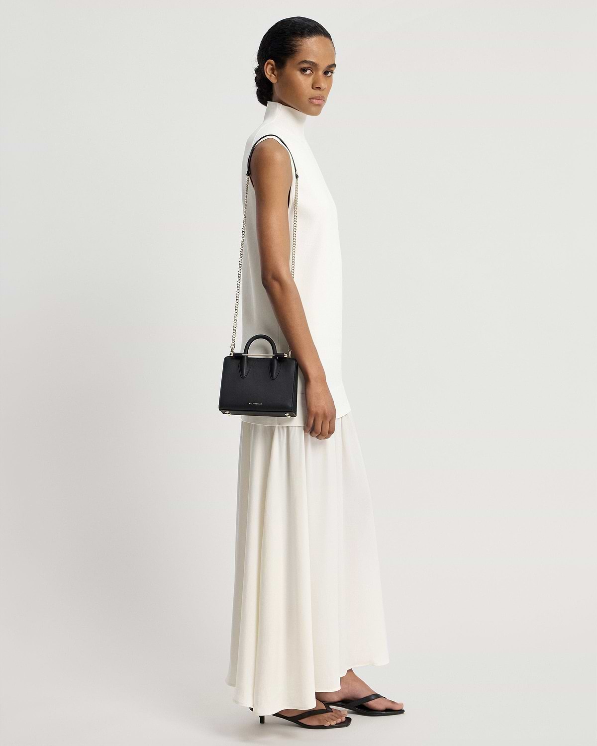 Model in a white sleeveless dress carrying a black nano tote with chain strap.