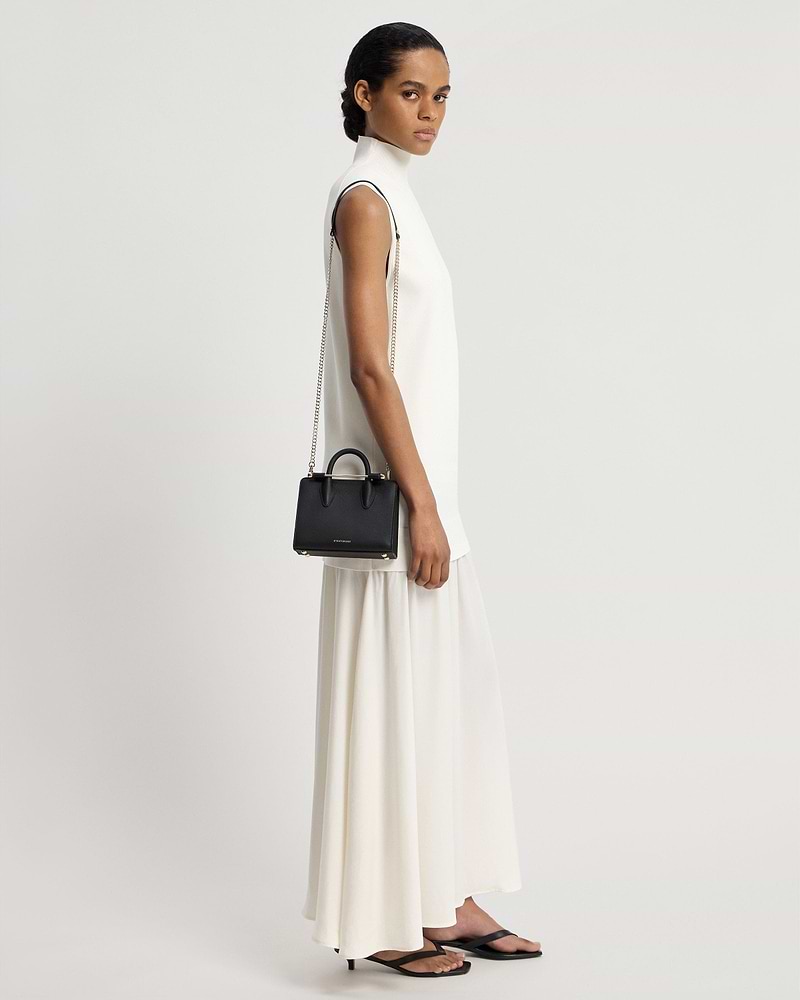 Model in a white sleeveless dress carrying a black nano tote with chain strap.