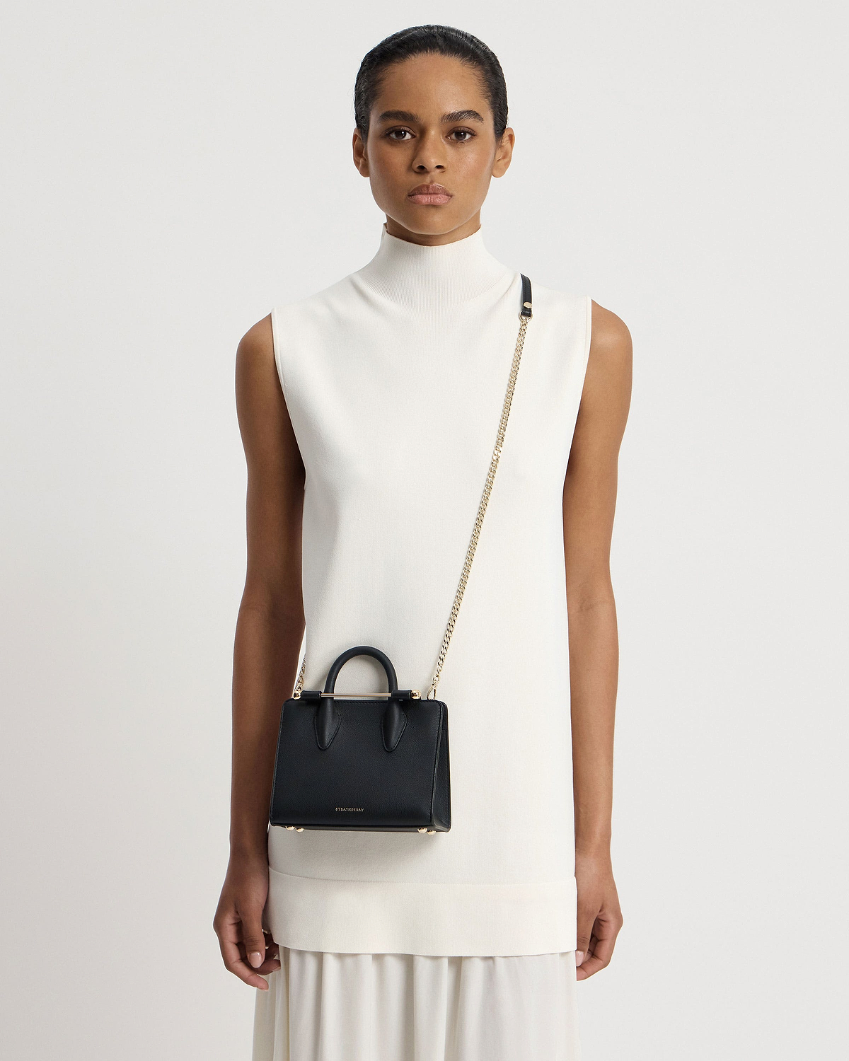 Model wearing white sleeveless dress with black Strathberry Nano Tote crossbody bag.