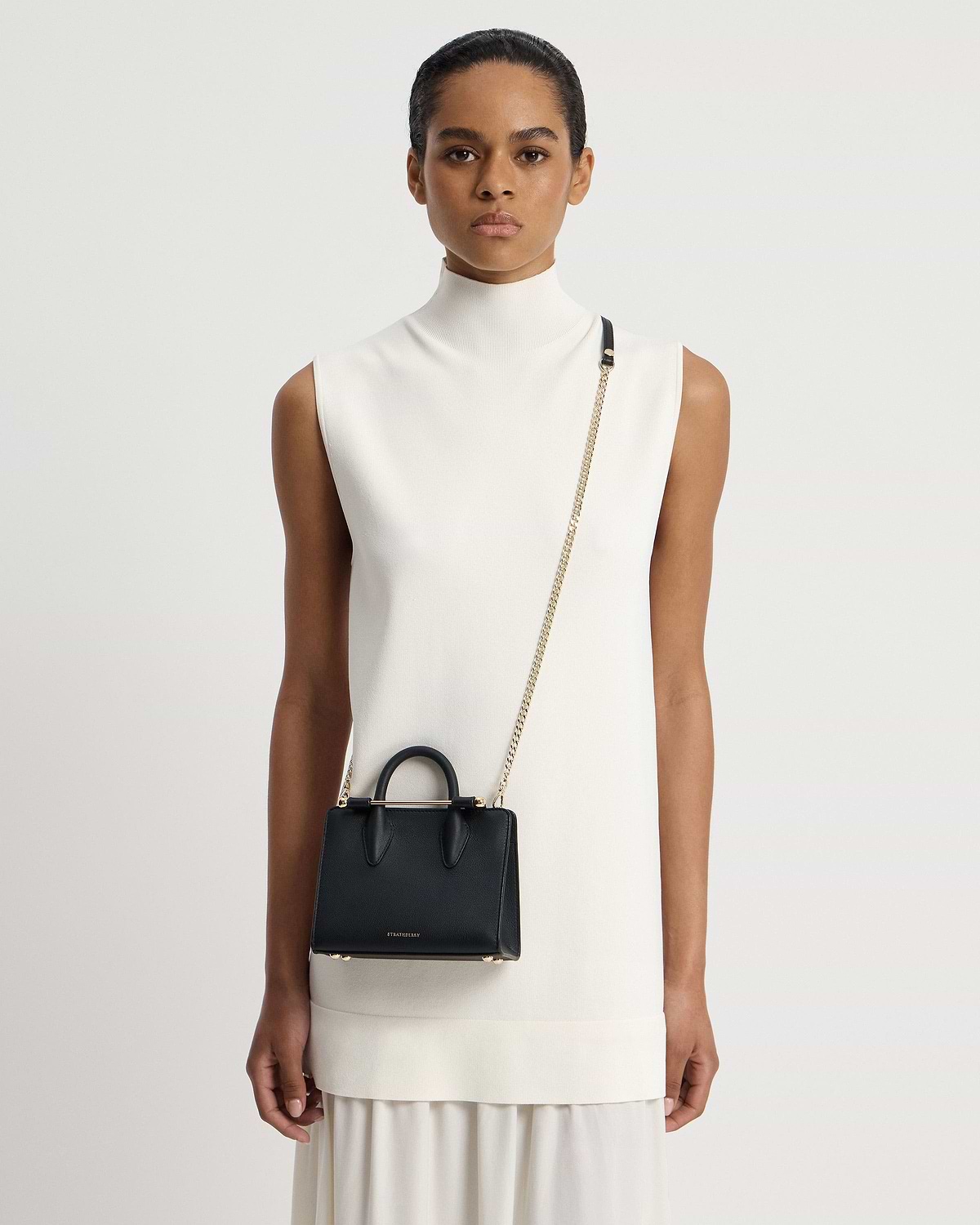 Model wearing white sleeveless dress with black Strathberry Nano Tote crossbody bag.
