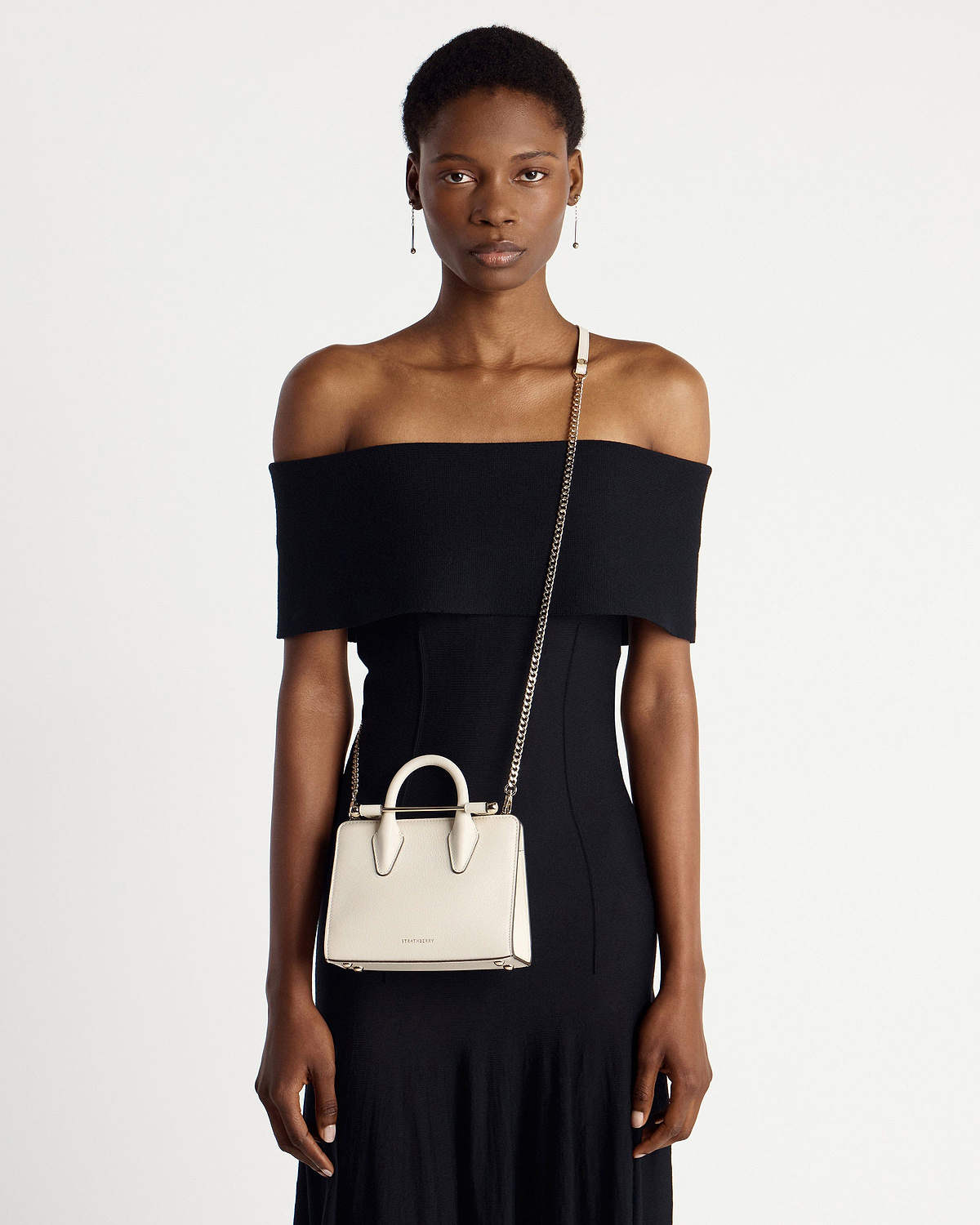 Model wearing vanilla Strathberry nano tote with chain strap and top handles.